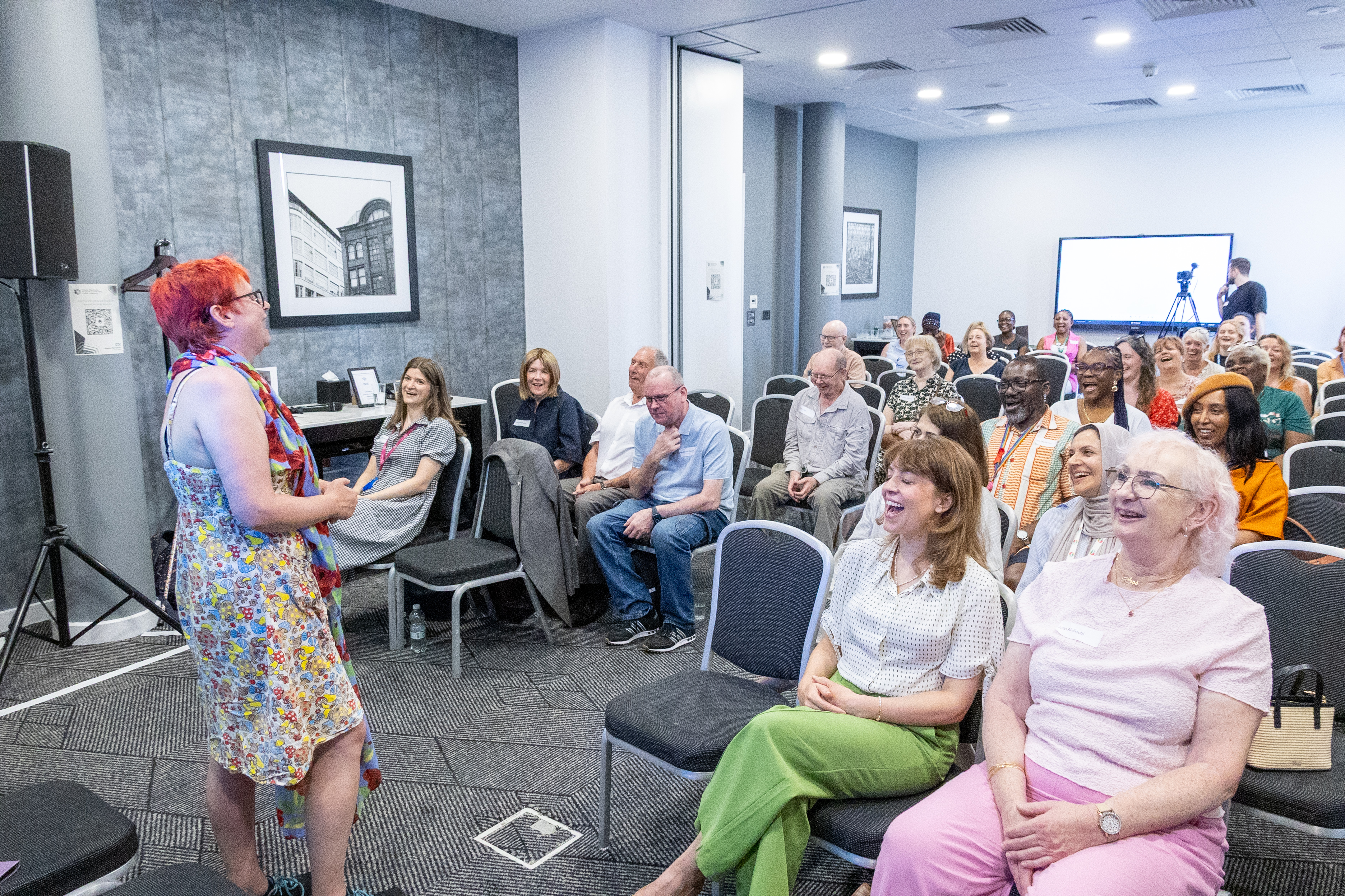 26 Delegates at the conference seated and joining in on a post break pick me up 'Laughter yoga therapy with Caroline Jone' with enthusiastic laughing expressions on faces