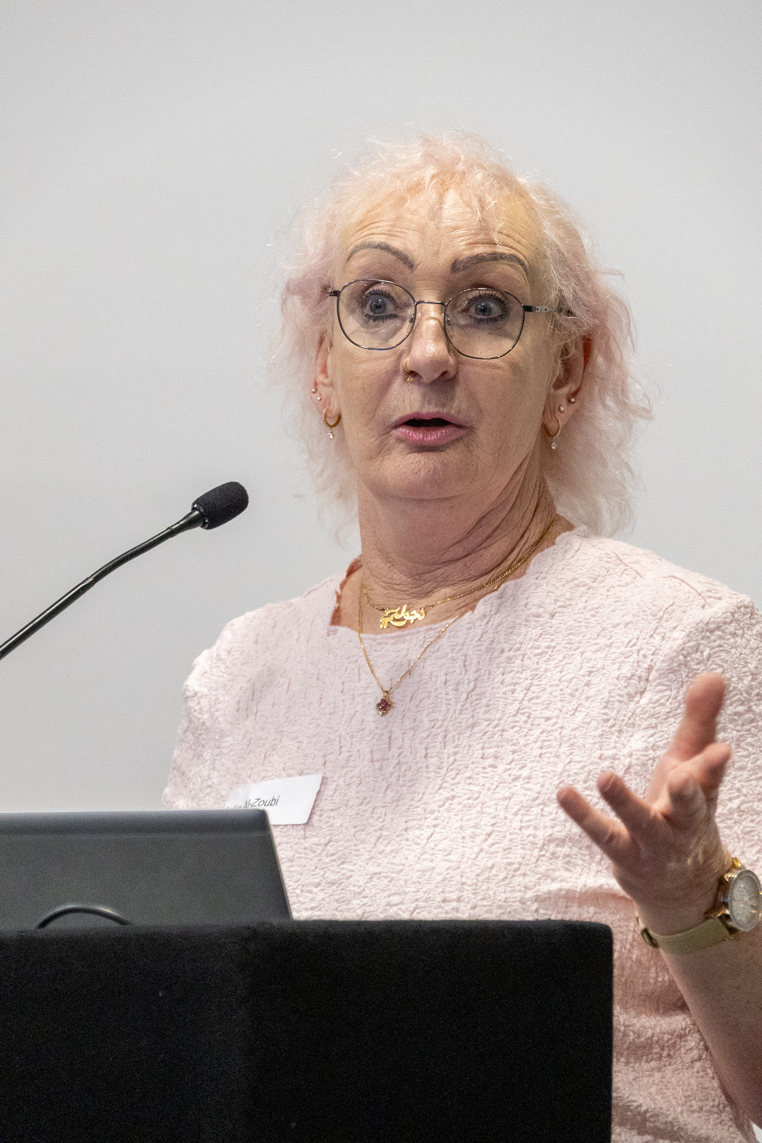 36 Julie stood at the front presenting at a conference behind a podium wearing a pink top and glasses