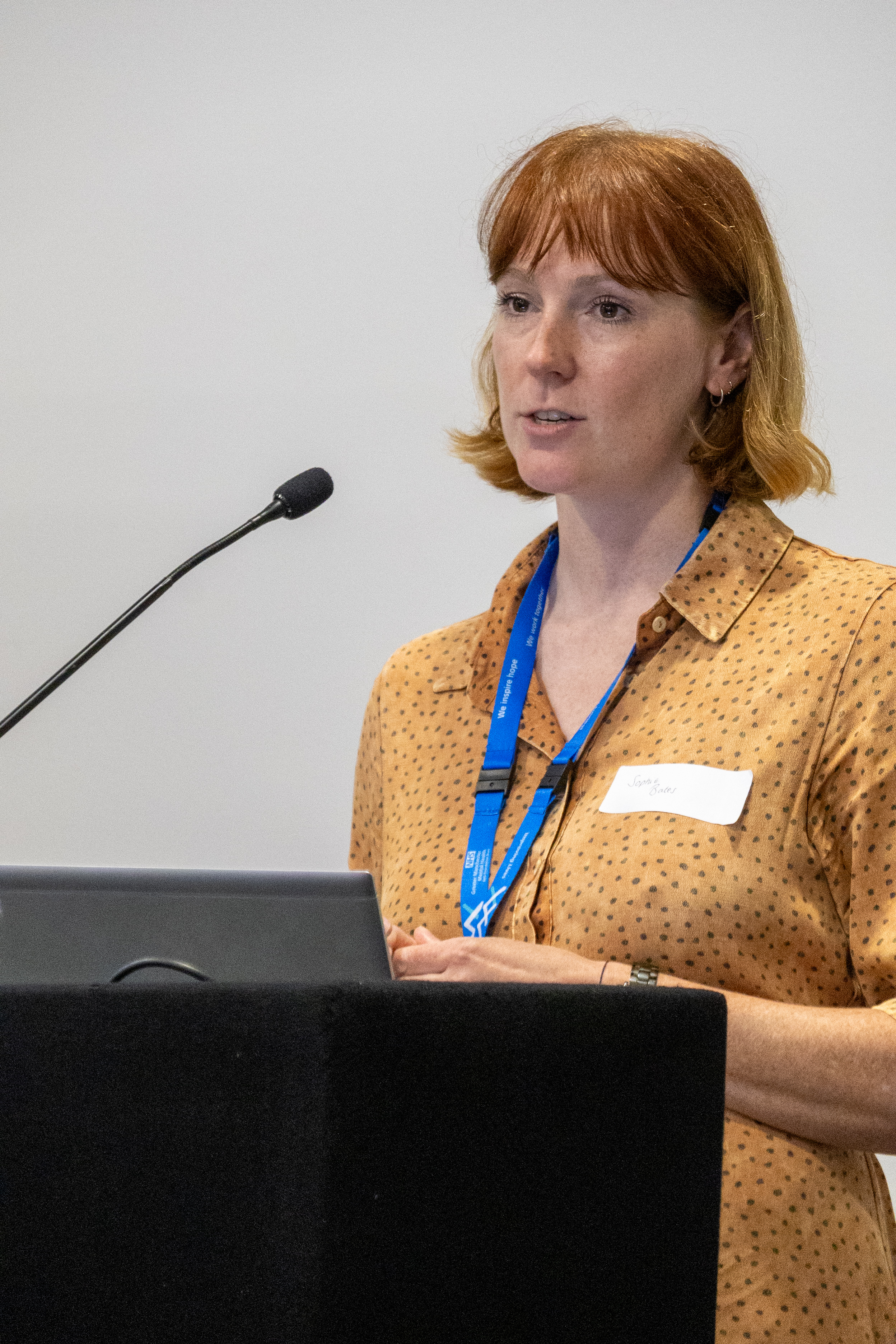 38 Close up of Sophie Bates standing at the front presenting at a conference wearing an orange dress and blue lanyard