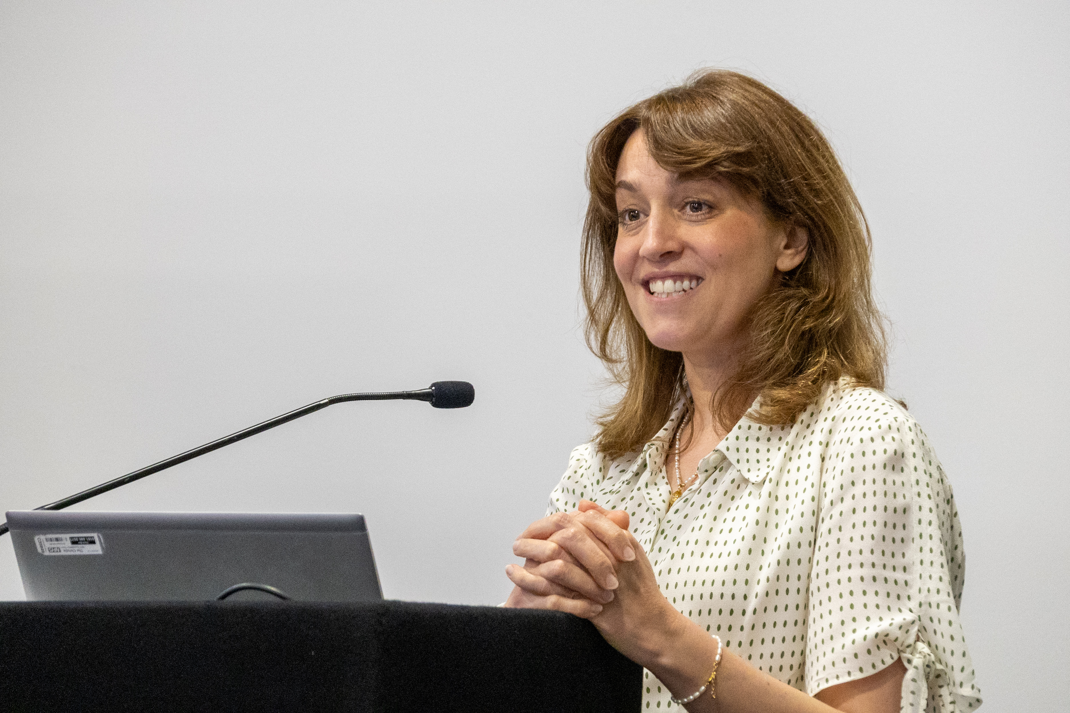 42 Clare Garnsey stood presenting behind a podium at a conference with a laptop in front of her and hands together smiling at the audience