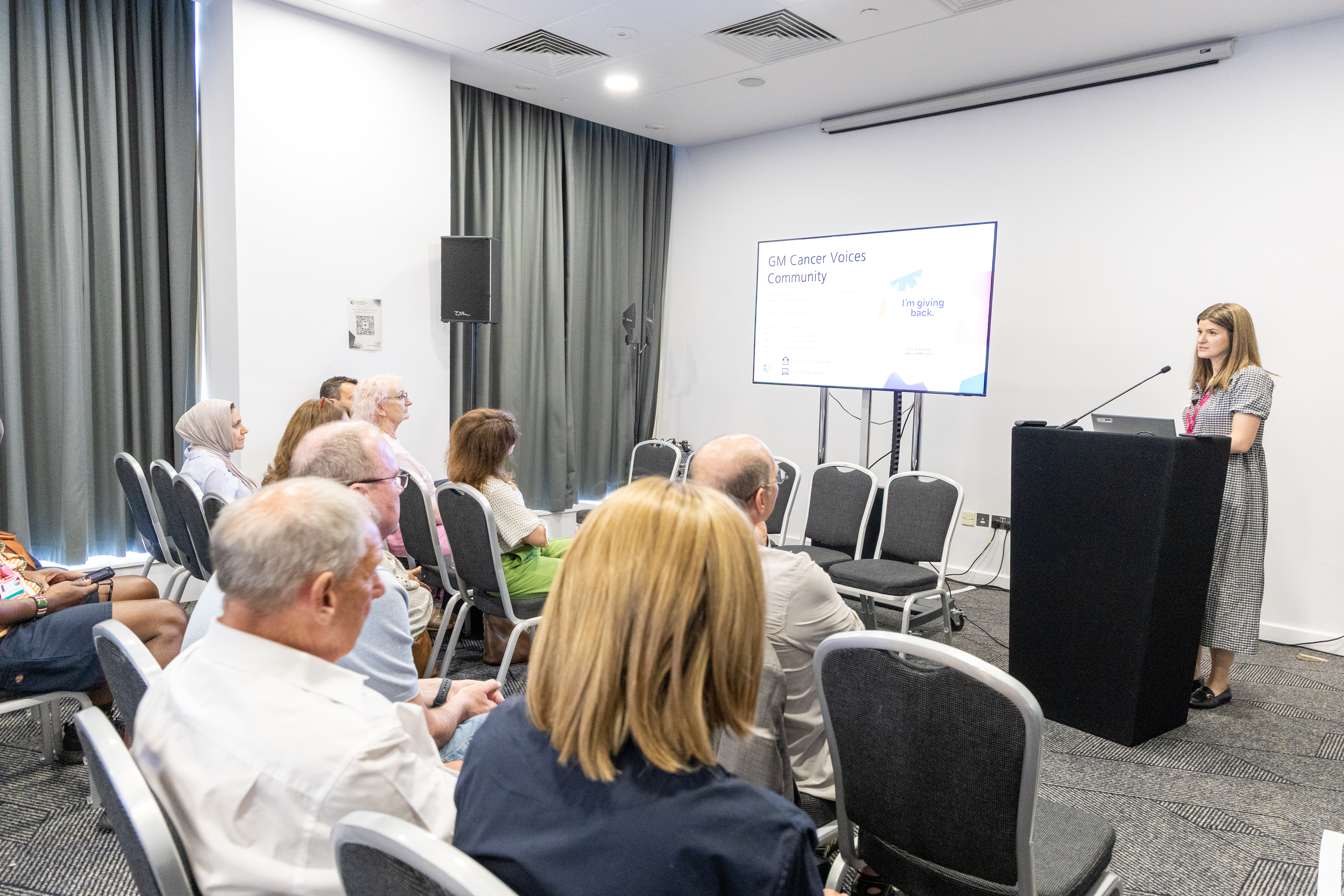 45 Naomi the Patient and Public Involvement and Engagement (PPIE) Manager stood at the front of a conference room presenting behind a podium