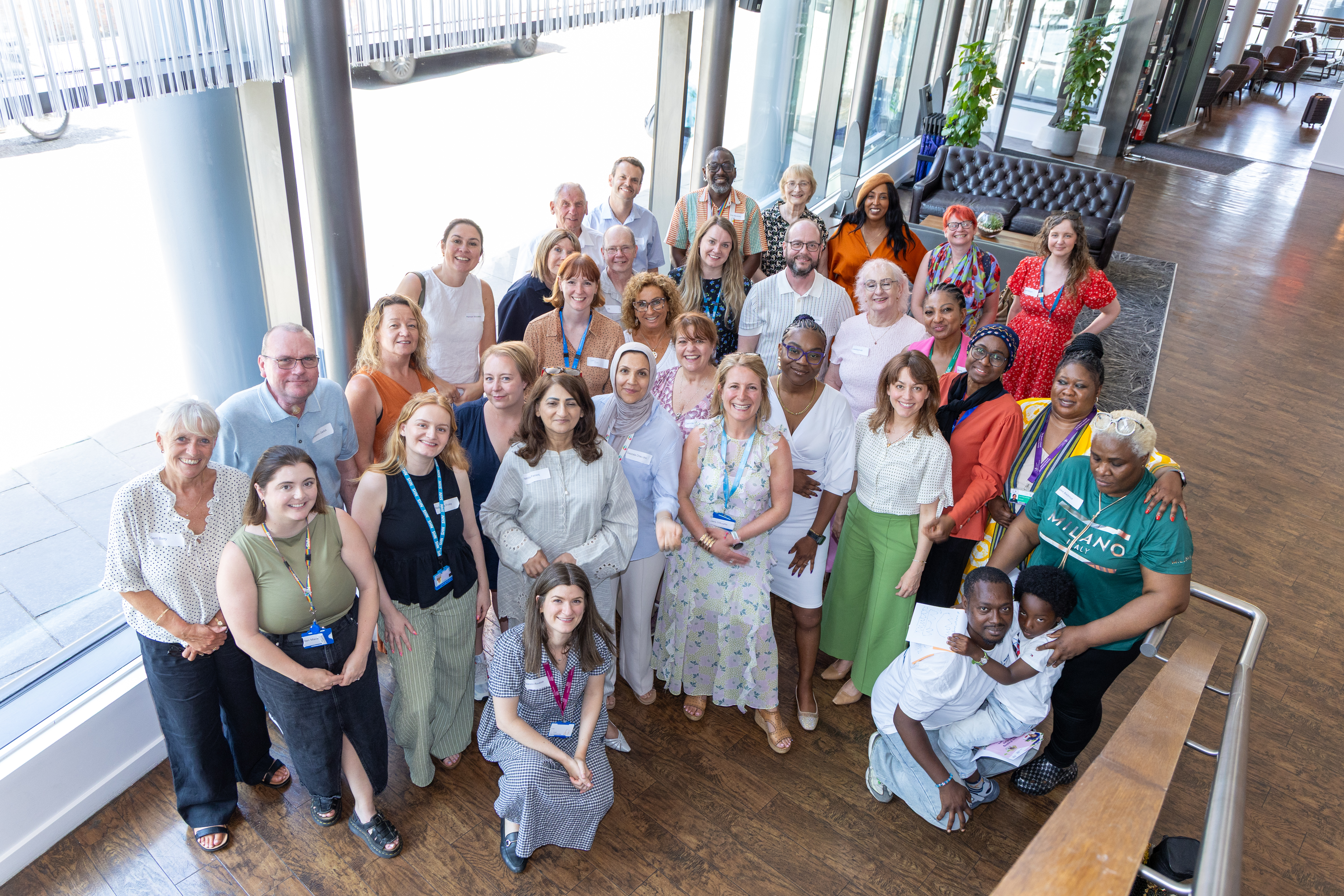 47 A group of people smiling in a bright indoor space with large windows.