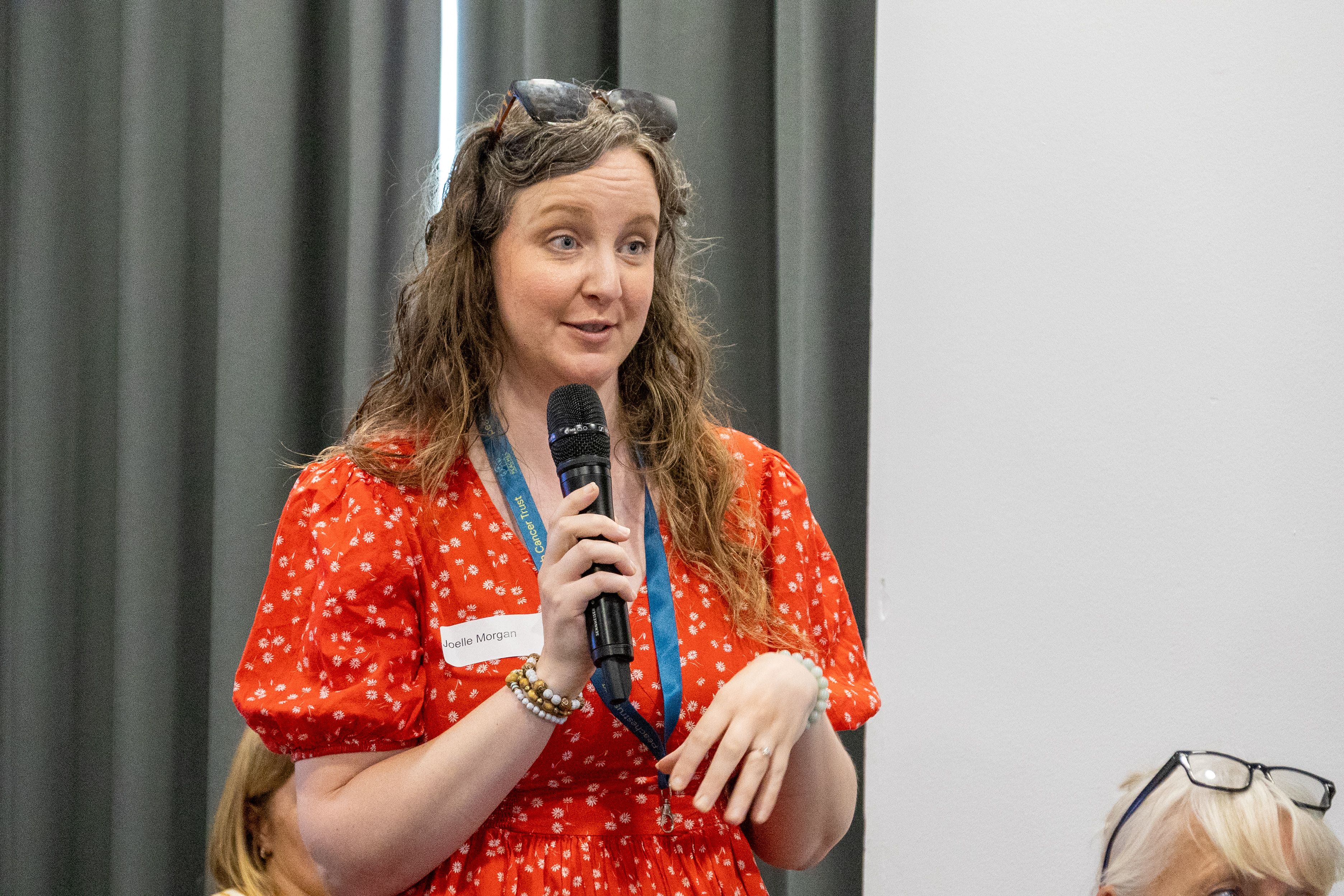 6 Joelle from Peaches Womb Cancer Trust holding a microphone speaking to the audience at a conference.