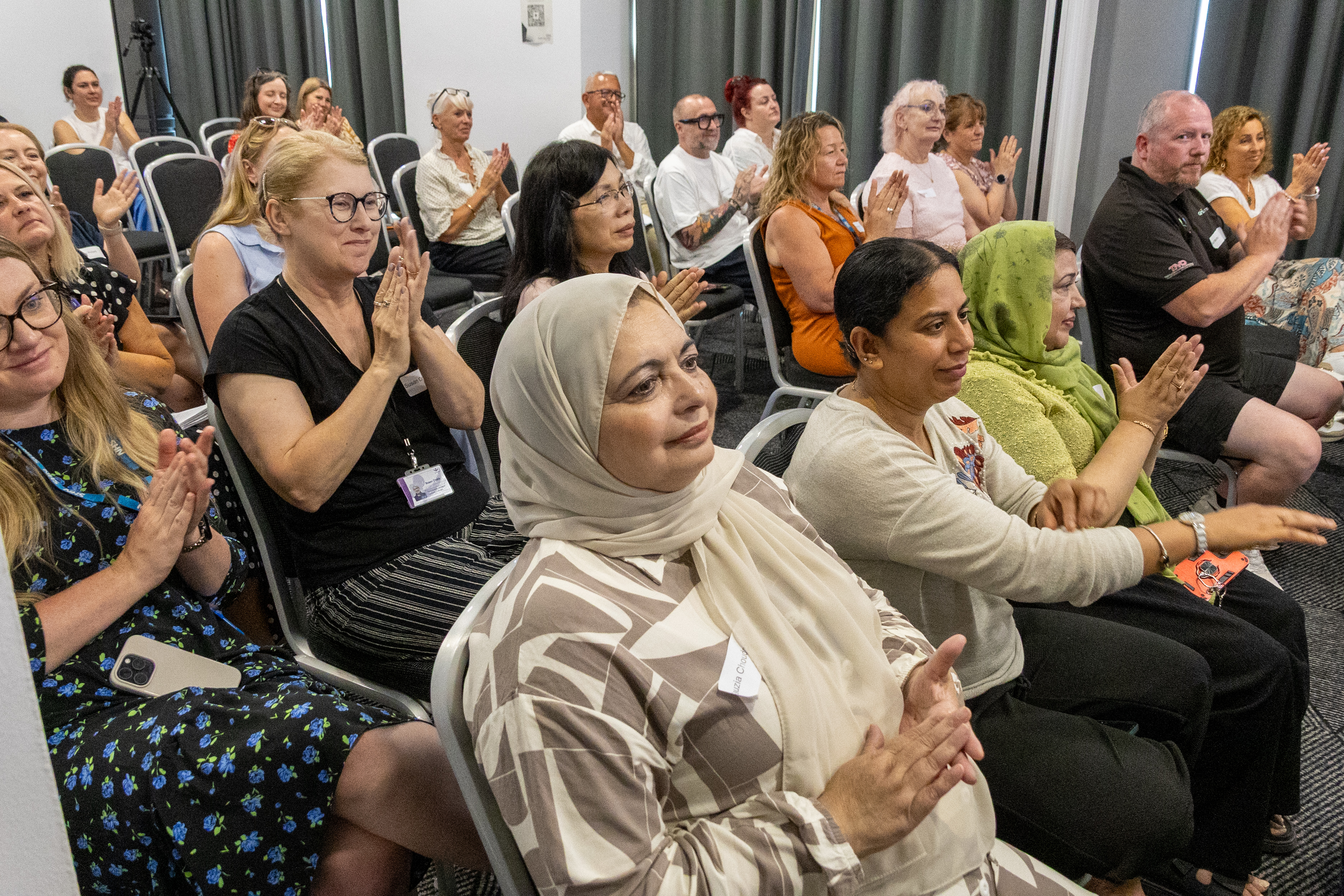8 A diverse group of people seated in rows, attentively listening and applauding during a presentation at a conference
