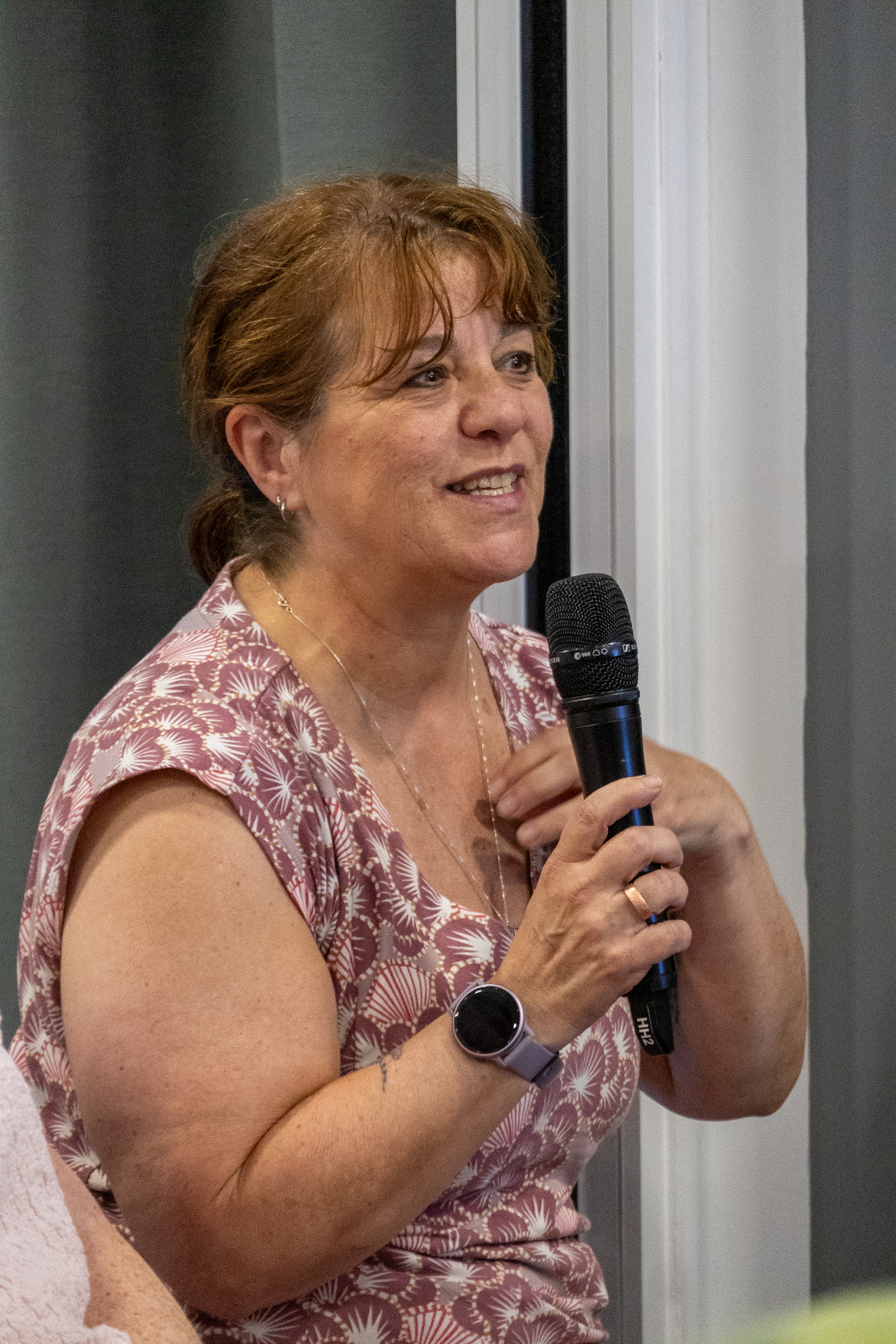 9 Lady holding a microphone with one hand and other hand on her chest speaking with a smile to a conference room of delegates.