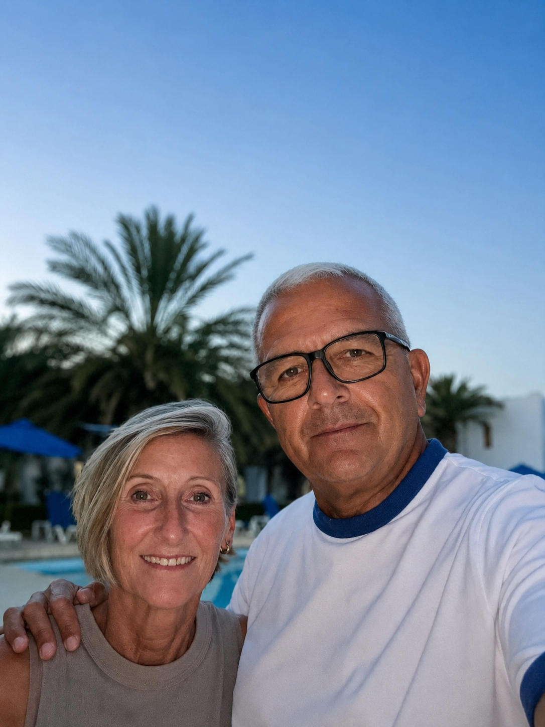 Gill and Stuart a white couple in their 60s on holiday with a blue sky and palm tree in the background