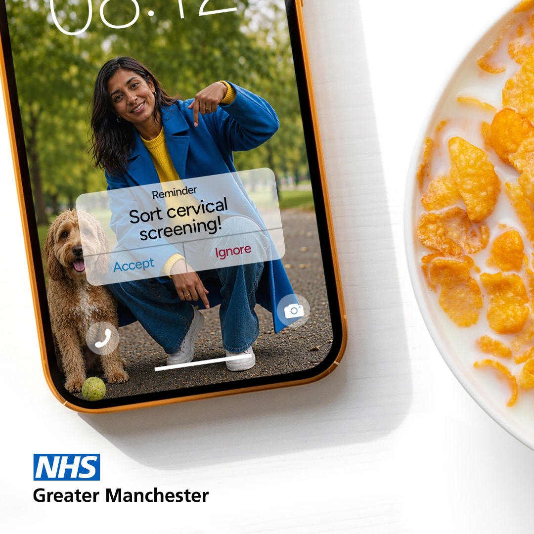 A breakfast table with a bowl of cornflakes and a mobile phone the screen saver features a woman crouched down with a dog and the words Book Cervical Screening Accept/ Reject. She is pointing at the word Accept
