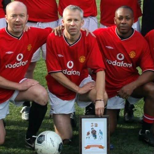Pete Smart centre with two team mates in his red Manchester United football kit crouching down for a photo