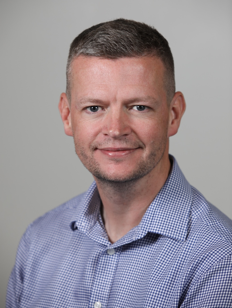 The late Professor John Moore a white man with short hair wearing a blue shirt.
