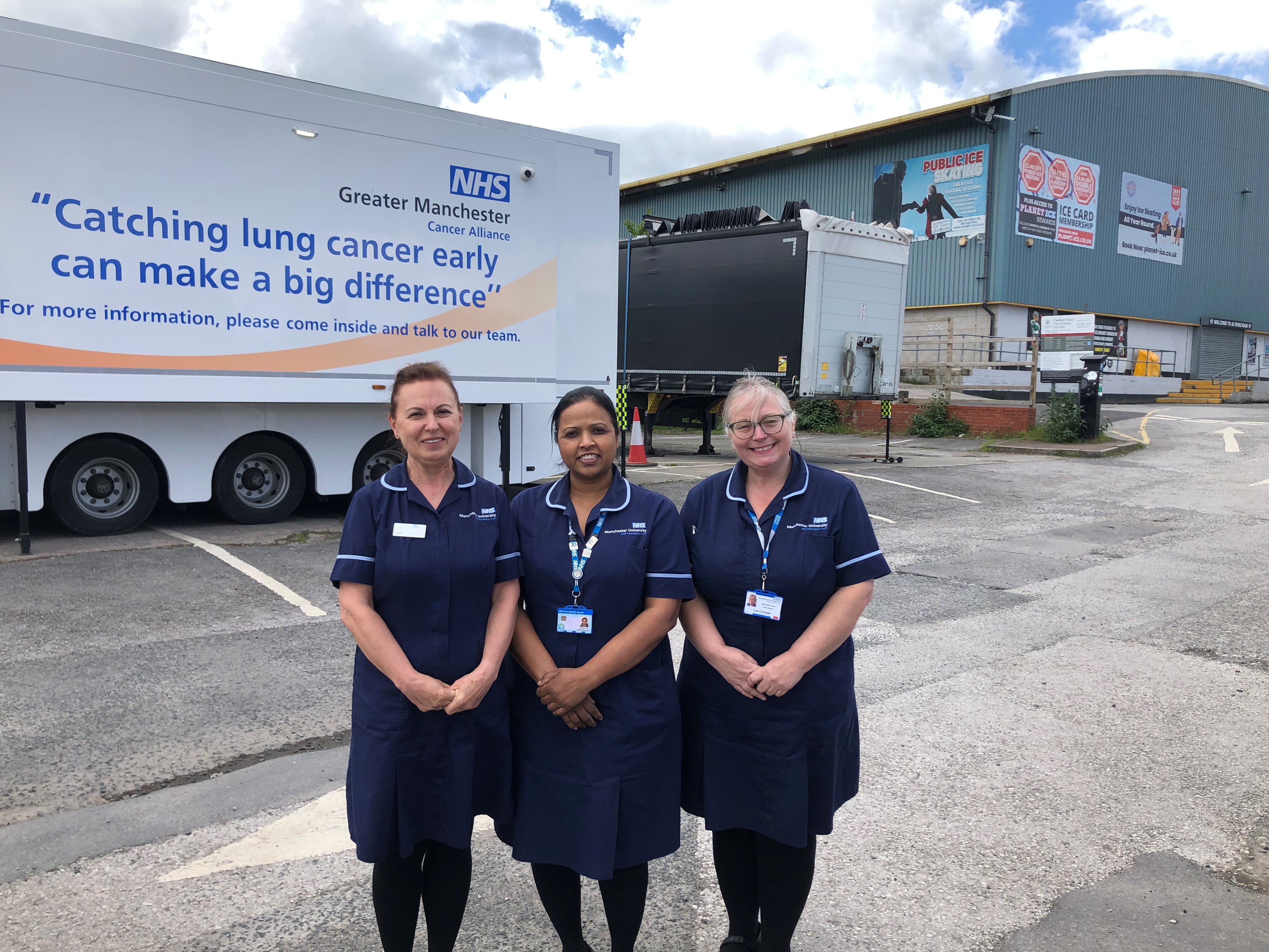 Three nurses stand in a car park in front of a mobile clinic with the words Finding lung cancer early can make a big difference written on the side