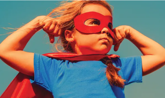 A girl in a superhero cape and mask showing her muscles